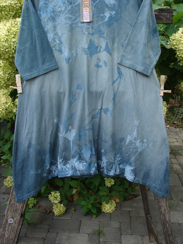 Barclay NWT Wander Tunic Tee Shadow Blossom Mottled Grey Green Size 0, featuring a nature-inspired pattern at the hem, three-quarter sleeves, and a rounded neckline, displayed on a rustic wooden frame outdoors.