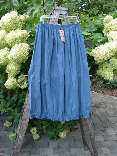 Barclay NWT Batiste Airy Lawn Skirt Unpainted Echo Blue Size 0, with an elastic waistband and gathered hem, hangs on a clear hanger outdoors, showcasing its lightweight cotton batiste fabric.