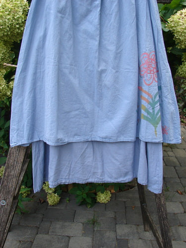 Barclay NWT Batiste Two Story Shaunting Skirt in Sky, displayed on a wooden stand outdoors, showcasing its light-blue tiered design with a side floral print, highlighting its elegant, flowing double-layered cotton structure.
