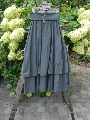 Barclay NWT Batiste Fold Over Stardust Tier Skirt Atlas Grey Size 0 displayed on a wooden stepladder, showcasing its full-length, tiered design and flowing silhouette amidst a garden setting.