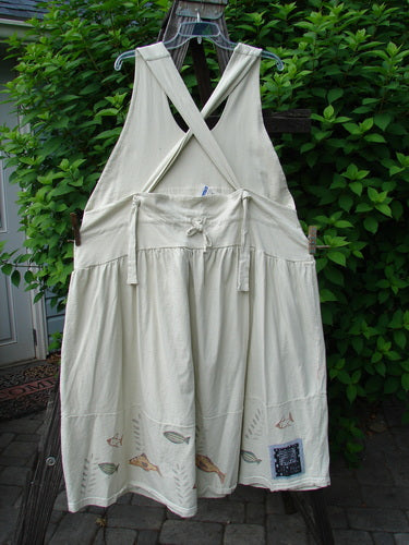 Image alt text: "1999 NWT Tadpole Jumper, a white dress on a clothesline, with fully adjustable shoulder straps, a huge sweeping hemline, and a criss-cross lower back. Features a downward yoked and slight empire double paneled waistline, two round bottomed pockets, and a single stripe pike theme paint. Perfect condition, made from organic cotton. Bust 40 and open, waist 50, hips 60, length 46 to 52 inches. From the Summer Collection of 2000. Blue Fish Clothing by Jennifer Barclay."