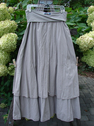 Barclay NWT Batiste Fold Over Stardust Tier Skirt Moon Rock Sand Size 0 hanging outdoors, showcasing its light-gray, tiered design and A-line flair, surrounded by greenery and cream flowers.