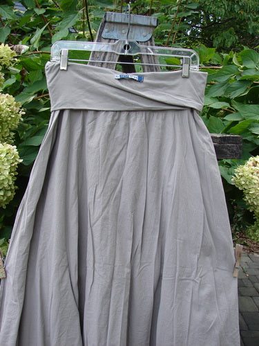 Barclay NWT Batiste Fold Over Stardust Tier Skirt Moon Rock Sand Size 0 draped in soft folds on a hanger, showcasing its tiered, A-line silhouette against garden foliage.