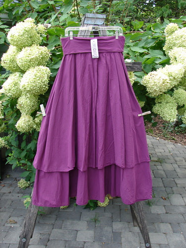 Barclay NWT Batiste Fold Over Stardust Tier Skirt Tyrian Berry Size 0, flowing with two-tiered lightweight fabric, displayed outdoors on a wooden stand, surrounded by lush hydrangeas, showcasing its A-line flair and generous sweep.