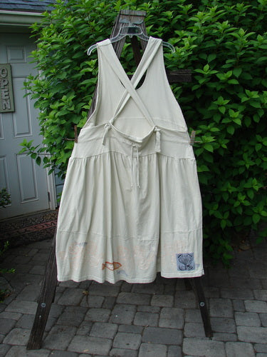 Image alt text: "1999 NWT Tadpole Jumper, a white dress on a clothesline, with fully adjustable shoulder straps, a huge sweeping hemline, and a downward yoked and slight empire double paneled waistline. Features two sweet round bottomed pockets and a single orange pike theme paint. Length is 46 to 52 inches. Perfect condition. Blue Fish Clothing by Jennifer Barclay."