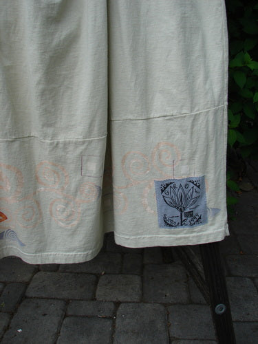 A close-up of a white sheet with a flower drawing, part of the 1999 NWT Tadpole Jumper. Made from organic cotton, it features adjustable shoulder straps, a criss-cross lower back, and round bottomed pockets. Bust: 40, Waist: 50, Hips: 60, Length: 46-52 inches.