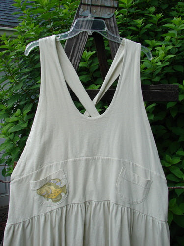Image alt text: A white dress with a fish on it, featuring fully adjustable shoulder straps, a huge sweeping hemline, and a downward yoked and slight empire double paneled waistline. The dress also has a drawcord criss-cross lower back, two sweet round-bottomed pockets, and a single gold fish theme paint.