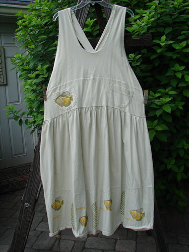 A white dress with a yellow fish design on a clothesline. Adjustable shoulder straps, sweeping hemline, and a criss-cross lower back. Features a gold fish theme paint and the Blue Fish signature patch. Bust 40, waist 50, hips 60, length 46-52 inches. Vintage 1999 NWT Tadpole Jumper.