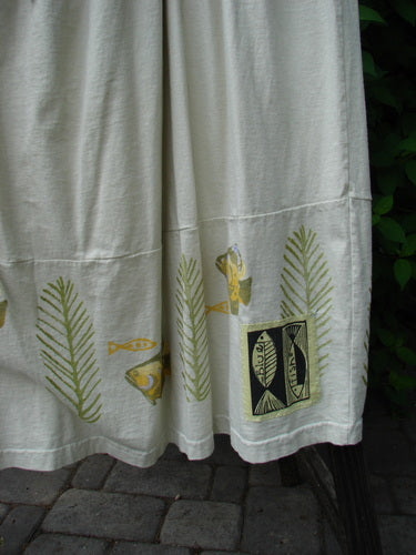 Image alt text: "1999 NWT Tadpole Jumper with fish and leaf design on white towel fabric, featuring adjustable shoulder straps, criss-cross lower back, and round bottomed pockets."