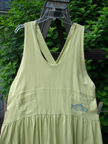 A green tank top with a fish on it, part of the 1999 NWT Tadpole Jumper Single Bass Moon Earth Citron collection. Made from organic cotton, it features adjustable shoulder straps, a sweeping hemline, and a criss-cross lower back. With a yoked and empire waistline, round-bottomed pockets, and a bass and moon theme paint, this jumper is a unique vintage piece from Blue Fish Clothing.