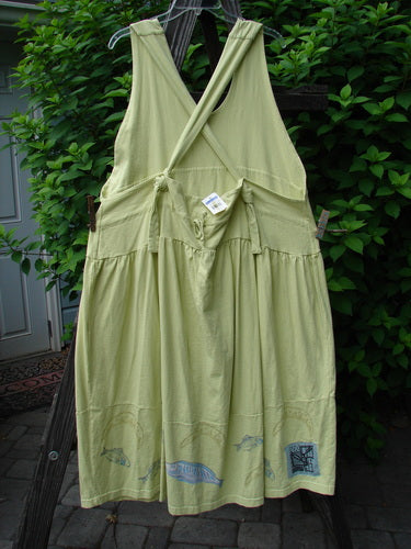Image alt text: "1999 NWT Tadpole Jumper dress on clothes line, featuring adjustable shoulder straps, sweeping hemline, crisscross lower back, empire waistline, round bottomed pockets, and bass and moon theme paint."