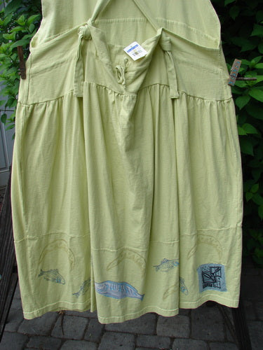 A green skirt with a fish design on it, part of the 1999 NWT Tadpole Jumper collection. Made from organic cotton, it features adjustable shoulder straps, a criss-cross lower back, and round bottomed pockets. Perfect condition.