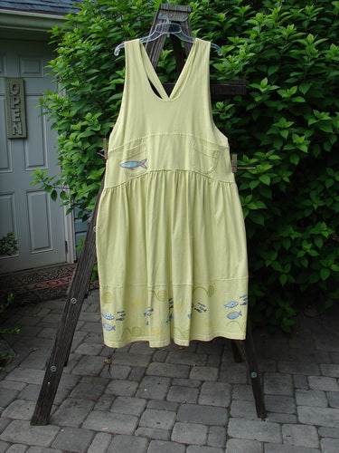 A yellow dress with a fish on it, hanging on a wooden ladder. Adjustable shoulder straps, sweeping hemline, criss-cross lower back, and round bottomed pockets. Vintage 1999 NWT Tadpole Jumper Single Stripe Pike School Citron OSFA.