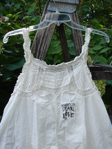 Magnolia Pearl NWT Embroidered Eyelet Cotton Clementine Tank True OSFA features lace-detailed straps, eyelet lower, pintucked bodice, and a signature patch, elegantly draped over a wooden easel.