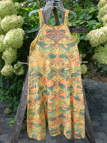 Magnolia Pearl NWT Cotton Fleece Lepidoptera Lana Tank Dress Butterfly Sunnies OSFA displayed on a weathered ladder in a garden, showcasing its sleeveless design and bright butterfly pattern amidst lush greenery.