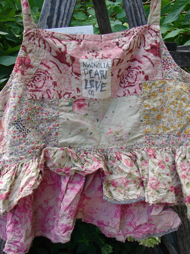 Magnolia Pearl NWT Quilted Catalina Tank Ragdoll Calico OSFA displayed on a rustic ladder, showcasing its floral patchwork design, ruffled hem, and signature Magnolia Pearl label against a lush garden backdrop.