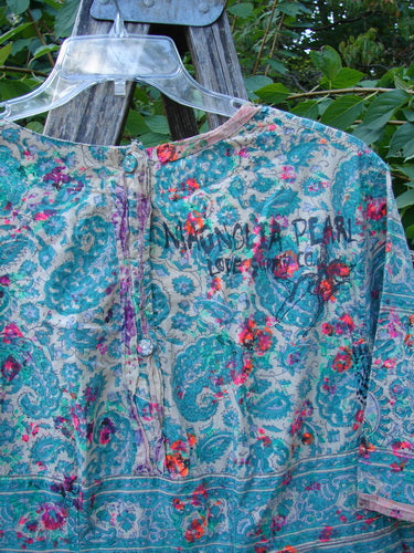 Magnolia Pearl NWT European Cotton Block Print Taigi Dress Demi OSFA hangs on a clear hanger, showcasing pintucks, pleats, and ric rack accents with triple rear buttons amidst a floral paisley print.