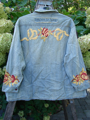 Magnolia Pearl NWT Embroidered Denim Isabel Shirt Washed Indigo OSFA displayed outdoors, draped over a ladder, highlighting ornate floral embroidery and distressed edges, capturing the store's vintage, expressive style.
