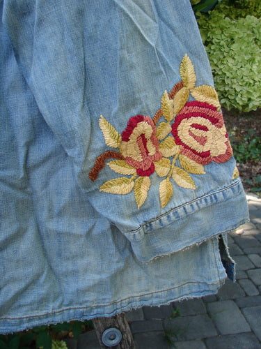 Magnolia Pearl NWT Embroidered Denim Isabel Shirt Washed Indigo OSFA features intricate rose embroidery on the sleeve, showcasing unique distressing and fading, symbolizing vintage-inspired individuality from Bluefishfinder.com.