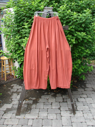 Image alt text: Barclay 4 Square Pant in Pumpkin, a pair of pants on a rack, made from Light Weight Organic Cotton. Unique bottom cut creates a 3D diamond shape from the knee down. Waist 32-42, Hips 72, Inseam 27, Length 45.