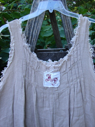 Magnolia Pearl Heavy Gauze Embroidered Signature Farm Love Overall Natural OSFA, featuring frayed edges, embroidered white patch, and unique raglan detailing, hanging against a lush green backdrop.