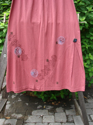 1996 Dubuffet Skirt Tumble Stone Ember Size 2: A skirt on a clothes rack with a pink pattern. Classic 1996 abstract theme paint. A-line lower with pleated triangular side panels adorned by painted buttons. Waist 28-50, hips 50, length 42.