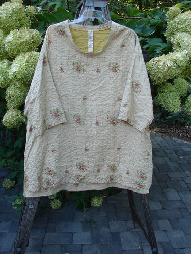 Magnolia Pearl European Cotton Quilted Hi Low Frances Top Vintage Rose OSFA: A cream-beige tunic with rose-pink floral embroidery, featuring a round neckline, three-quarter sleeves, and frayed edges, displayed outdoors.