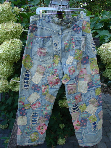 Magnolia Pearl NWT Denim Heavily Patched Miner Jean Garden Patch Washed Indigo OSFA, featuring distressed light-wash denim with vibrant, irregular floral patches, adjustable button fly, and unique stitchery, displayed outdoors among green foliage.