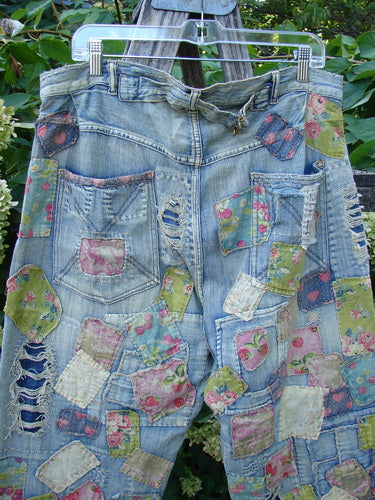 Magnolia Pearl NWT Denim Heavily Patched Miner Jean Garden Patch Washed Indigo OSFA displayed outdoors on a hanger, showcasing distressed denim richly overlaid with irregular floral and pastel cloth patches, emphasizing a unique upcycled style.