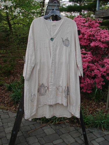 1999 NWT Cream and Sugar Coat Tea Time Teadye OSFA displayed on a wooden rack, showcasing a V-shape neckline, oversized shell button, and varying lower drape with a tea time theme.
