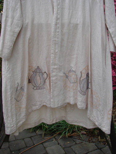 1999 NWT Cream and Sugar Coat Tea Time Teadye OSFA with teapot print, featuring an upward scoop front hem, V-shaped neckline, deep side pockets, oversized shell button closure, and varying lower drape.