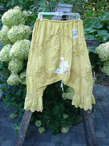 Magnolia Pearl NWT Embroidered Khloe Bloomer Golden Daffodil OSFA features loose-fitting, mustard-yellow harem-style pants with elastic waistband, lace trim, and patchwork accents, displayed on a hanger outdoors.