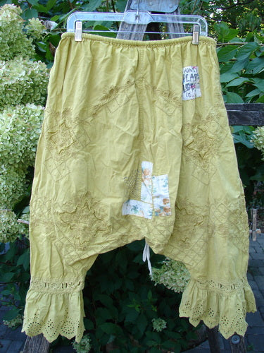 Magnolia Pearl NWT Embroidered Khloe Bloomer Golden Daffodil OSFA features vintage-style, loose, olive-green pantaloons with decorative eyelet ruffles, tonal embroidery, and floral patches, hanging outdoors on a plastic hanger.