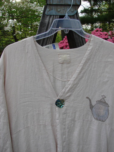 1999 NWT Cream and Sugar Coat Tea Time Teadye OSFA featuring a teapot design, displayed on a hanger outdoors, showcasing its unique drape, V-shaped neckline, and oversized shell button.