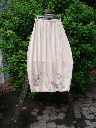 Barclay Little Lace Trim Skirt, a cream-colored skirt with a garden folly theme paint and a sweet laced hem circumference, hanging on a rack.
