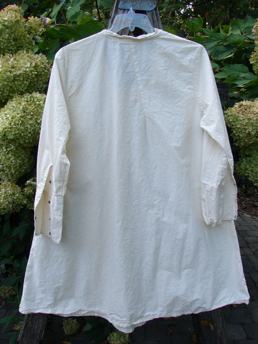 Magnolia Pearl Cotton Poplin Wabi Diagonal Tunic Natural OSFA, displayed from the back on a wooden hanger outdoors, features unique diagonal seams, raglan edgings, and long sleeves with tiny snaps.