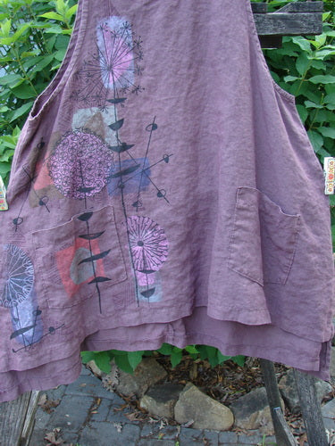 Barclay Linen Two Pocket Shirttail Pinafore Starburst Plum Wine Size 1 features an A-line flair, rounded neckline, double exterior pockets, and a flowy shape with a distinct starburst pattern.