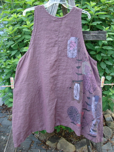 Barclay Linen Two Pocket Shirttail Pinafore Starburst Plum Wine Size 1 displayed outdoors, showcasing its A-line flair, rounded neckline, and double exterior pockets, highlighting its flowy shape and unique starburst pattern.