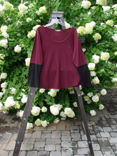 A red shirt with contrasting long sleeves on a wooden rack with white flowers. Barclay Contrast Bell Sleeve Top in Burgundy, Size 2.