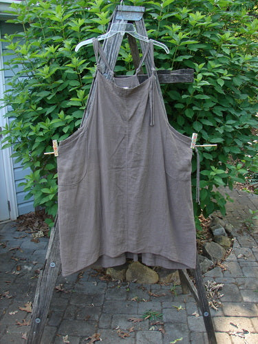 Barclay Linen Rayon Pucker Side Pocket Apron Jumper Unpainted Bark Size 1 displayed on a wooden stand, showcasing adjustable straps, double front rounded pockets, and a softly textured pucker rib.