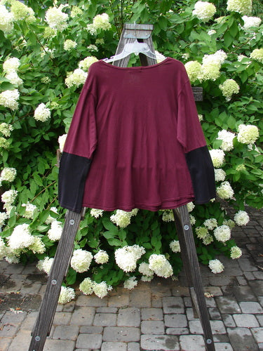 Image alt text: Barclay Contrast Bell Sleeve Top in Burgundy, featuring a red shirt on a wooden stand with contrasting lower long sleeves.