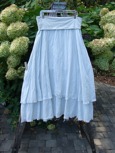 Barclay NWT Batiste Fold Over Raglan Silhouette Skirt Unpainted Dew Size 1 draped over a wooden ladder, showcasing its airy, tiered cotton layers and frayed edges in a garden setting.