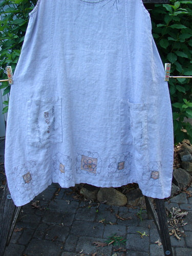 Barclay Linen Pocket Pinafore Mosaic Floral Lavender Size 0, featuring sectional panels, A-line flair, scoop neckline, and double drop exterior mosaic floral pockets, crafted from lightweight linen, displayed on a stone walkway.