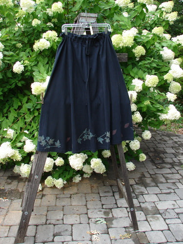 1993 Sweep Skirt Fall Leaves Black Size 1: A full swing skirt on a clothes rack. Panels create a sweeping shape with a gathered and ruffled waist. Painted falling leaf theme on the hem.
