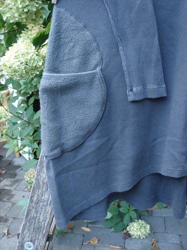 Barclay NWT Thermal Cloud Forest Pocket Tunic Unpainted Smoke Size 0 displayed on a wooden bench outdoors, showcasing its textured knit, rounded patch pocket, and long sleeves amidst lush greenery and hydrangeas.