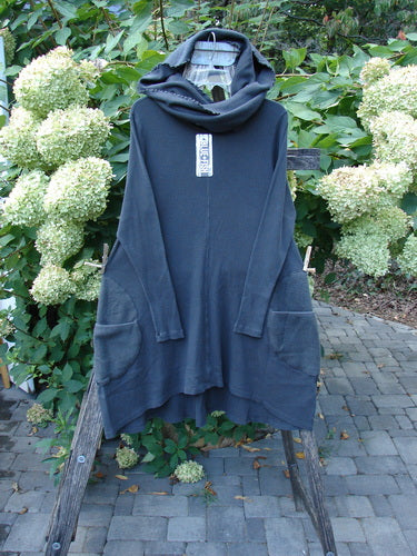 Barclay NWT Thermal Cloud Forest Pocket Tunic Unpainted Smoke Size 0, features a loose cowl hood, long sleeves, and large front pockets, displayed draped over a wooden frame amidst garden foliage.