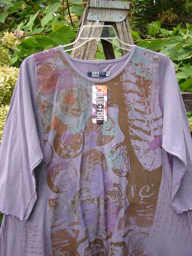 Barclay NWT Three Quarter Sleeve Color Wheel Tunic Many Moons Violet Size 0, featuring abstract circular and floral prints, hangs on a ladder, showcasing lettuce-edged sleeves and a rounded neckline.