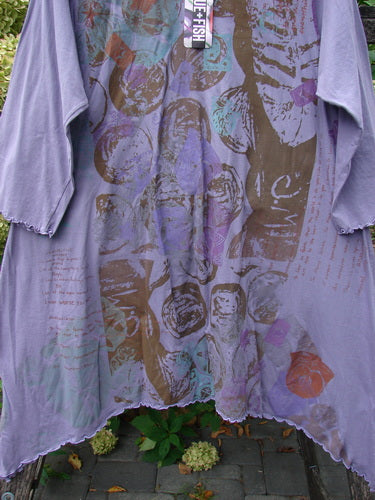 Barclay NWT Three Quarter Sleeve Color Wheel Tunic Many Moons in Violet Size 0, features an abstract fossil-like print, lettuce edges, and asymmetrical cut, displayed outdoors with hydrangea blooms beneath.