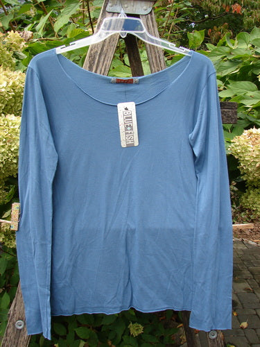 Barclay NWT Batiste Raw Edge Layering Tee Unpainted Blue Bird Size 1 displayed on a clear hanger, showcasing long sleeves, a wider raw neckline, and rolled edgings against a garden backdrop.