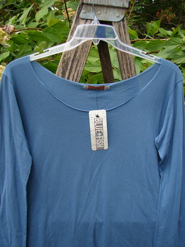 Barclay NWT Batiste Raw Edge Layering Tee Unpainted Blue Bird Size 1 displayed on a clear hanger, featuring long sleeves, a wide raw cut neckline, and rolled edgings, perfect for creative expression.